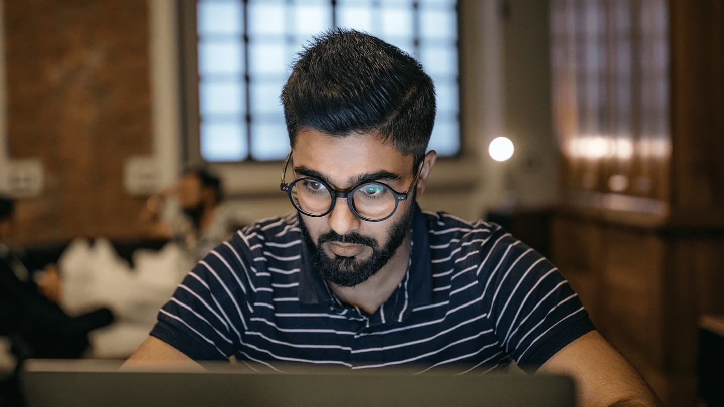 A male with black-frame glasses, black and white striped shirt looks at computer screen